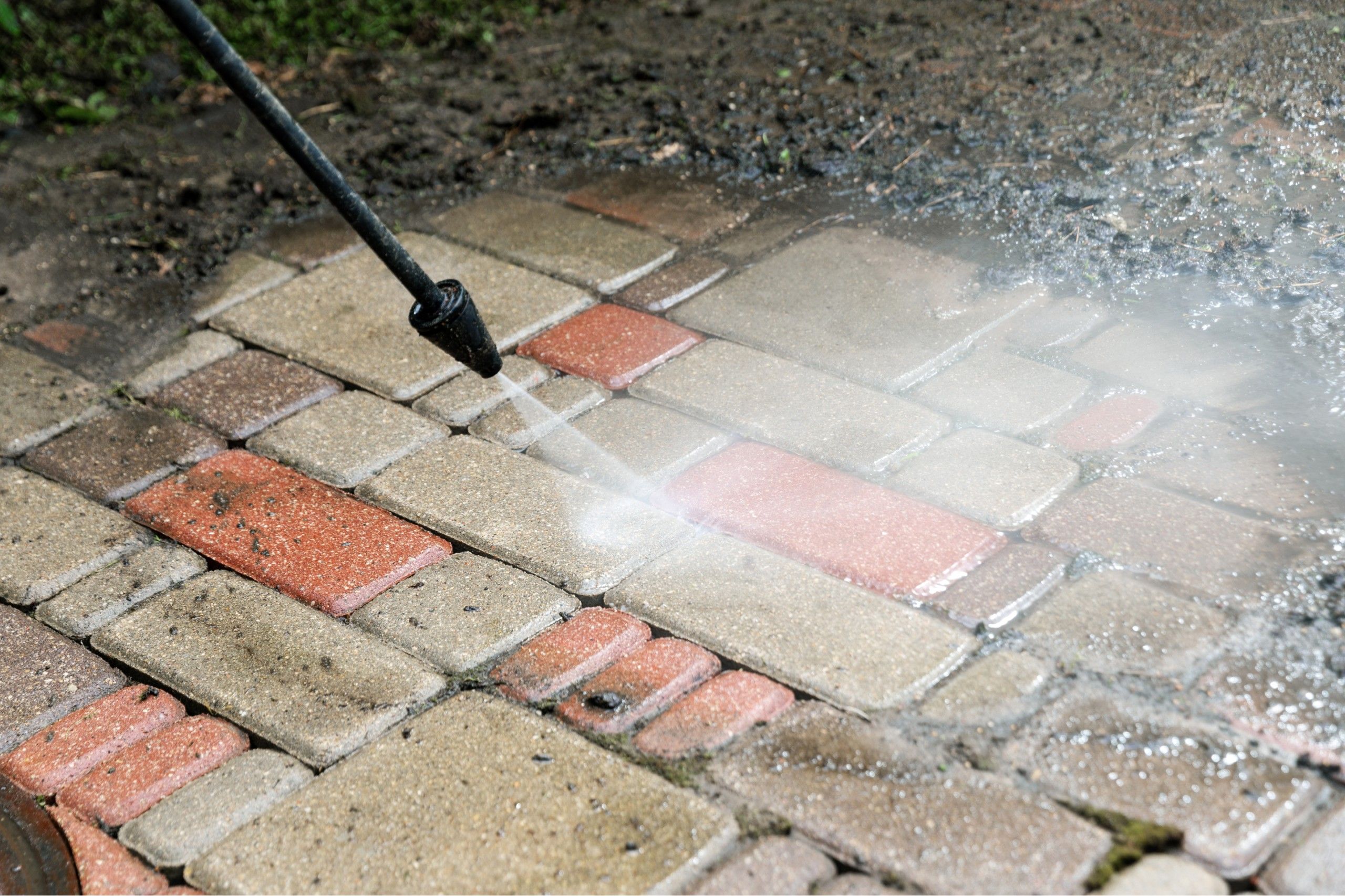 Pressure washer wand cleaning a dirty brick paver walkway